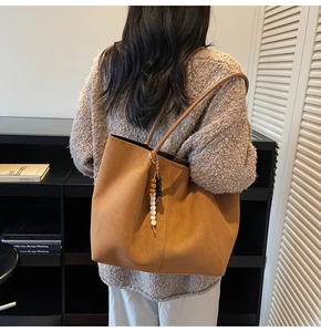 Détail du sac cabas en daim camel avec pendentif en perles de bois porté par un mannequin