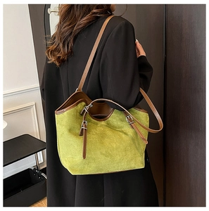 Detail of green suede tote bag with brown leather trim and metallic buckle accents