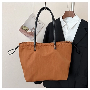 Detail of a brown large tote bag featuring drawstring closure and leather straps