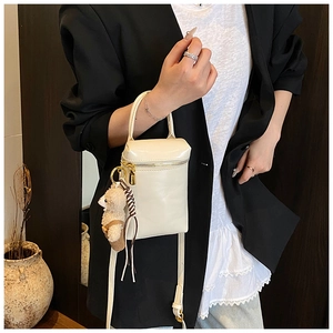 Mini sac à main blanc crème avec breloque ours en peluche porté sur un blazer noir