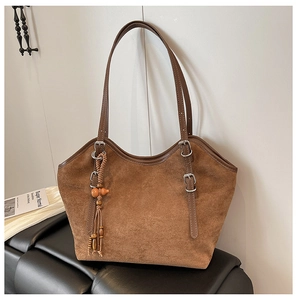 Detail of brown suede tote bag featuring silver buckles and a unique beaded tassel charm