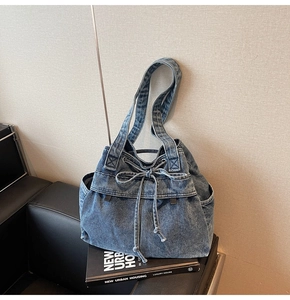 Close-up of a blue denim bucket bag with drawstring bow and dual wide shoulder straps