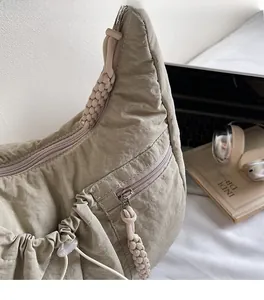 Detail of khaki nylon pleated bag with drawstring and woven zipper pull on a desk