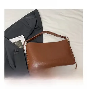 Vue détaillée d'un sac vintage marron avec bandoulière tissée et œillets sur un lit blanc