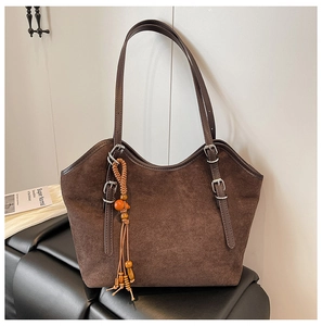 Close-up of brown suede tote bag featuring adjustable leather straps and beaded tassel charm