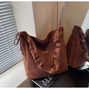 Detail of brown suede tote bag with drawstring accents and embossed pocket tag