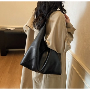 Detailed view of black minimalist tote bag with diagonal stitching on soft beige trench coat