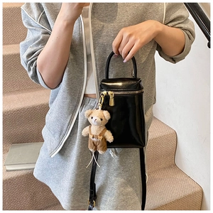 Détail du mini sac bandoulière en cuir verni noir avec un accessoire de breloque ours en peluche