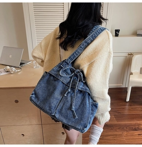 Detail of blue denim tote bag with drawstring texture shown on a beige knit cardigan