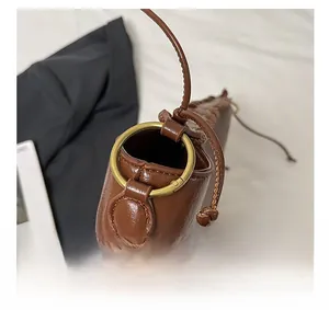 Détail du sac en cuir marron montrant l'anneau en métal bronze et les coutures