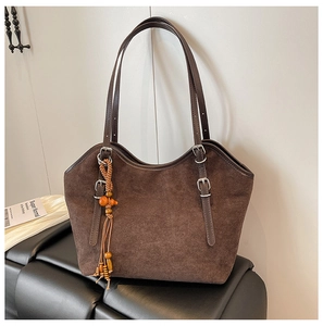 Detail of a large brown suede tote bag with fringe charm and adjustable straps