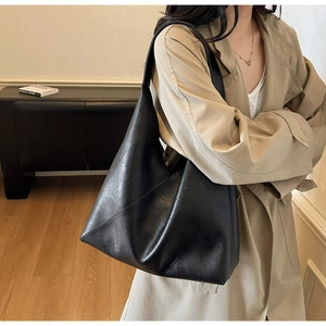 Minimalist black leather tote bag with wide strap worn by model in a modern room