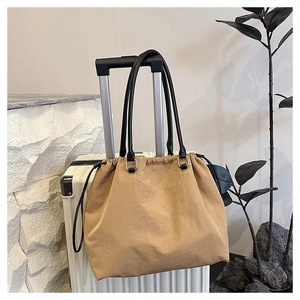 Detail of camel nylon tote bag with drawstring closure on a white suitcase