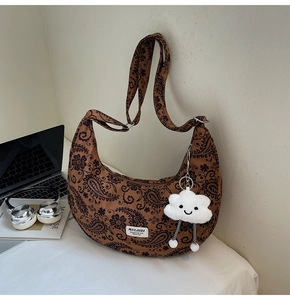 Braune Paisley-Halbmondtasche mit Plüschanhänger in einem modernen Lifestyle-Szenario