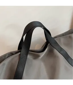 Detailansicht der schwarzen Nylongriffe und Nahttextur der grauen Reisetasche