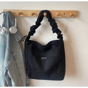Detail of black suede tote bag featuring a ruched drawstring strap and front pocket