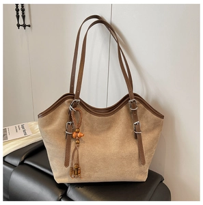 Detail of suede tote bag featuring a leather strap with silver buckle and beaded tassel