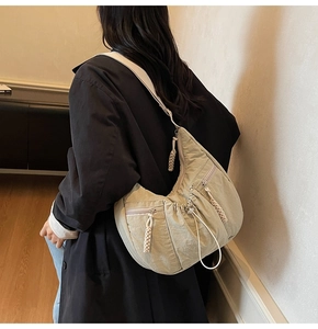Detail of light coffee pleated crescent bag with woven zipper pull and wide strap