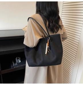 Détail du grand sac cabas noir en daim avec perles en bois porté avec un trench-coat classique