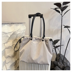 Detail of light gray drawstring tote bag hanging on a white suitcase for travel