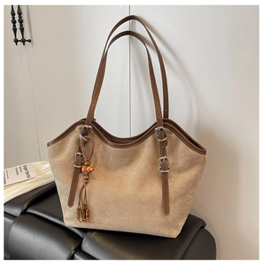 Detail of beige suede tote bag featuring brown leather strap and decorative tassel charm