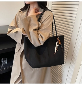 Détail du grand sac cabas noir en daim avec un charm décoratif à pampilles en perles