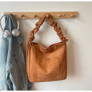 Detail of a brown suede tote bag featuring a ruched shoulder strap and front pocket