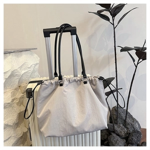 Detail view of a beige nylon tote bag with black handles attached to a white suitcase