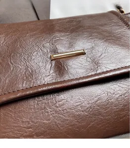 Detail view of deep brown leather texture and golden metal bar hardware on the shoulder bag