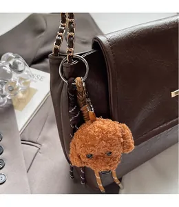 Close-up of brown teddy bear plush charm with woven strap on a leather handbag