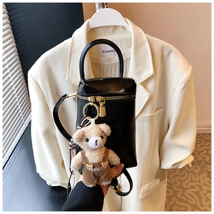 Détail du sac à bandoulière cylindrique noir avec fermeture éclair dorée et charm d'ours