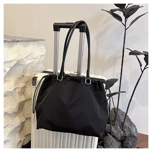 Black nylon tote bag with drawstring closure hanging on a white suitcase handle