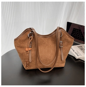 Detail of a brown suede tote bag featuring a handmade woven tassel charm and silver buckle
