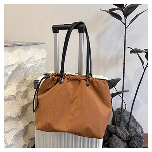 Caramel drawstring tote bag hanging on a suitcase handle for travel convenience
