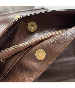 Detail of golden magnetic buckle on retro brown leather tote with striped fabric lining