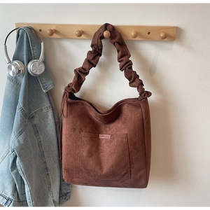 Detail of brown suede bucket bag with unique gathered shoulder strap and front pocket