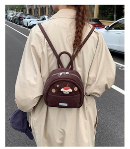 Outdoor shot of a small brown corduroy backpack with a cute dog patch on a model