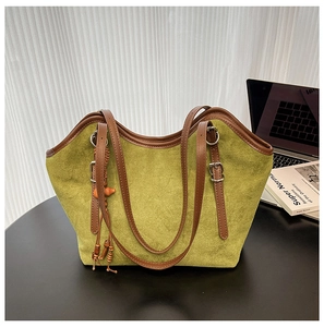 Detail of green suede tote bag with brown leather handles and decorative tassel
