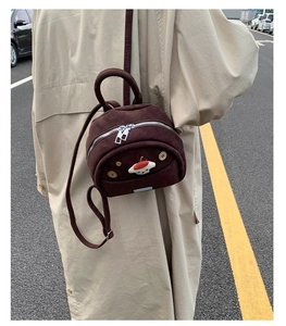 Close-up of a mini brown suede backpack featuring mushroom patches and dual silver zippers
