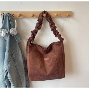 Detail of dark brown suede tote bag featuring a ruched shoulder strap and front pocket