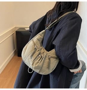 Detail of light olive pleated crossbody bag showing textured fabric and zipper compartments