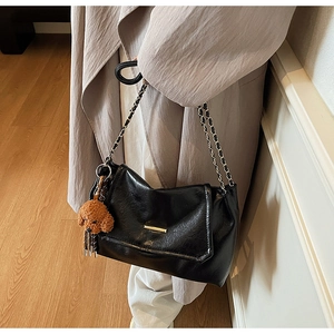Detail of black glossy shoulder bag with gold metal buckle and brown teddy charm