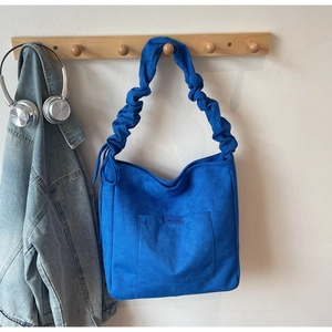Detail of blue suede shoulder bag with pleated strap and square pocket hanging on a wall