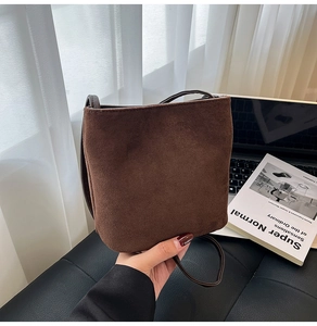 Close-up of minimalist dark brown suede bucket bag featuring sleek matte leather shoulder strap