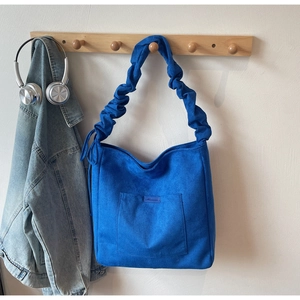 Detail of blue suede bucket bag with stylish ruffled strap hanging on wooden hook