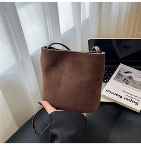 Detailed view of dark brown suede bucket bag texture and slender leather strap design