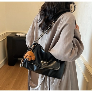 Detail of black vintage chain shoulder bag featuring a cute brown teddy bear charm