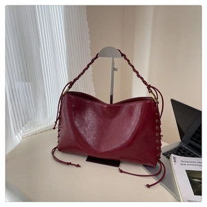 Détail du sac cabas bordeaux en cuir brillant avec anses tressées et anneaux dorés