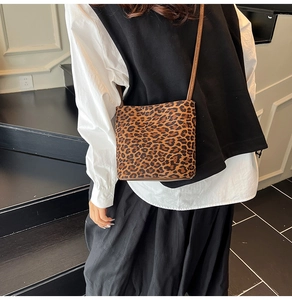 Detail of leopard print crossbody bucket bag with brown strap on a model indoors