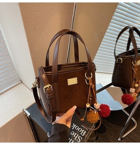 Detail view of dark brown suede bucket bag with gold hardware and colorful pompom keychain